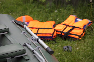 The board of a green inflatable boat with a paddle on the background of orange life jackets on the...