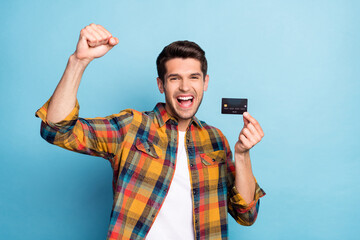 Portrait of attractive cheerful guy holding in hand bank card celebrating having fun deposit...
