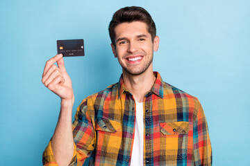 Portrait of attractive cheerful guy holding in hand black bank card savings deposit isolated over bright blue color background