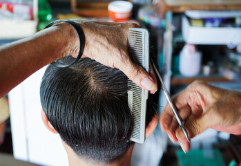 Fototapeta premium Closeup hands of hairsltylist and rear view of man having a hair cut by scissors and comb.