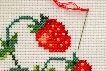 Red ripe strawberries embroidered with a cross-stich on a white canvas by hand. With a needle and...
