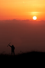 Silhouette of a man raised trekking sticks up at sunset