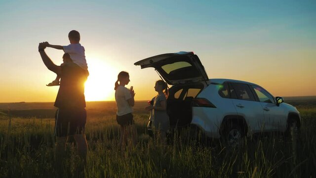 Silhouette the happy family. Four people, mother, father and two children are happy standing near the open trunk of a car at the sunset time. Concept of summer vacation and friendly family.