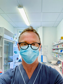 Authentic portrait of a male nurse wearing protective face mask and glasses in a medical supply room in a hospital.