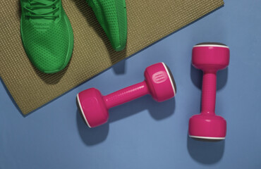 Green sport shoes, dumbbells and fitness mat on blue background. Workout concept. Top view.