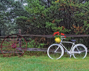 Fototapeta na wymiar An old white painted bicycle leaning on a split rail fence with an old wagon wheel doing the same.