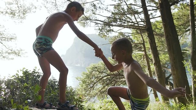 boy 10 years old helps little brother climb on path during summer vacation near the adriatic sea