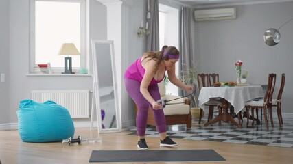 Funny obese woman using resistance band training indoors. Wide shot of Caucasian fat young sportswoman exercising with equipment at home. Sport and fun concept
