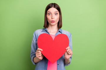 Photo of young girl amazed shocked hold paper heart feelings love isolated over green color...