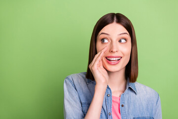 Photo of young girl happy positive smile hand near mouth whisper tell secret look empty space isolated over green color background