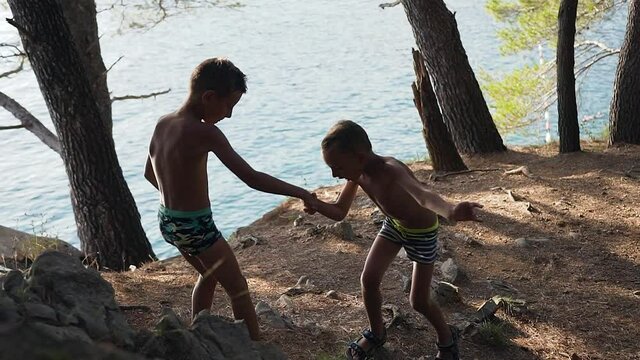 Adorable boy 8 years old helps little brother climb on path during summer vacation near the adriatic sea