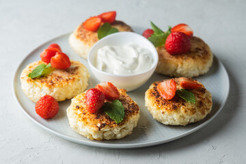 Cottage cheese pancakes with strawberries, mint and sour cream on a light background. syrniki. healthy dessert
