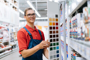 smiling construction store clerk standing near the color palette samples . - 443682000