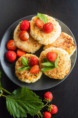 Cottage cheese pancakes with strawberries, mint and sour cream on a black background. syrniki. healthy dessert