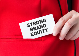 woman putting a card with text STRONG BRAND EQUITY in the pocket, hand close-up