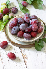 Obraz premium Seasonal food background. Ripe juicy plums in a bowl on a rustic wooden table. Copy space.