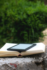 Open book and e-reader in a garden. Selective focus.