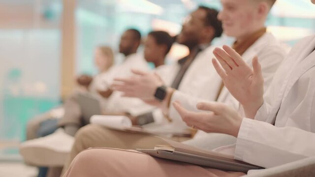 Side-view close-up of unrecognizable hands of medical students in white coats applauding to professor thanking for interesting lecture