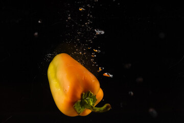 yellow bell pepper dropped into the water on a black background and a lot of bubbles