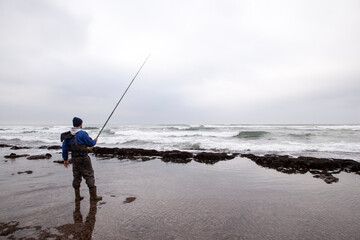 A fisherman standing on a rocky shore