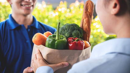 Asian delivery man in blue uniform sending grocery bag of food, fruit, vegetable to woman customer