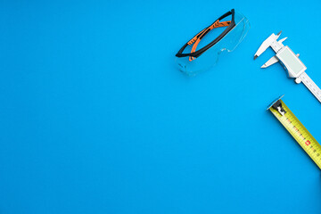 Technician's set of tools on solid coloured blue background including spectacles, caliper and tape...