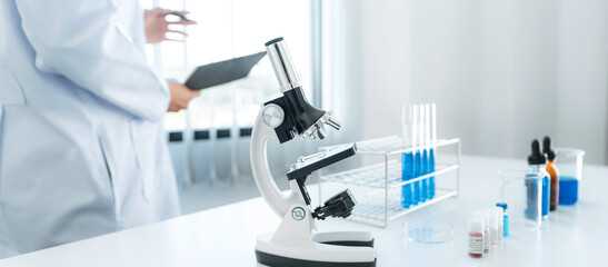 Scientist woman standing to reading result coronavirus vaccine on report after using microscope and test tube