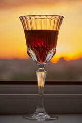 A glass of red wine on the windowsill against the background of the sunset.