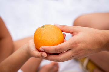 Madre pasando una naranja a la mano de su hija 