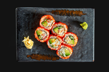 California sushi roll with crab, avocado, cucumber and tobiko caviar served on a plate with wasabi and ginger. Isolation on a black background. Japanese food