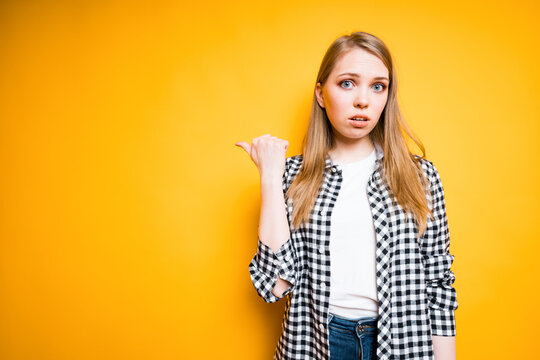 Beautiful displeased girl indignantly looks at the camera and shows her thumb to the side