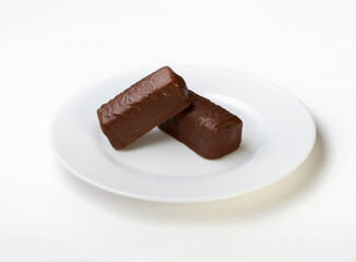 Glazed cottage cheese in milk chocolate on a white plate and a white background. Cottage cheese on a white background. Isolation.