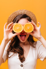 Lovely woman covers her eyes with oranges. Girl in straw hat showing tongue