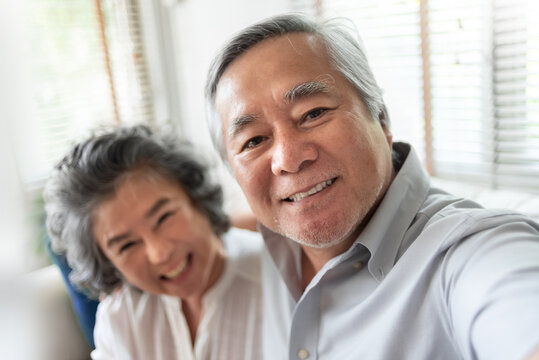 Happy smiling Asian Senior Couple in casual clothes taking selfie with smartphone at their home