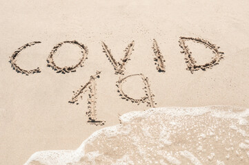 Sea wave sweeps inscription COVID 19 on a sandy beach