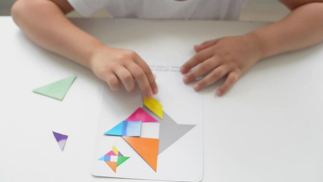 A preschooler girl sitting at the table collects a drawing from a geometric figure. the concept of early childhood development by montessori. a game of logic and imagination.