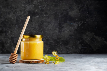 Summer linden fragrant honey in a glass jar with a spoon for honey on a gray background copy space