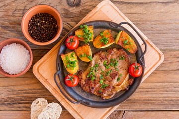 Roasted pork steaks in frying pan from neck meat with potato. wooden background.