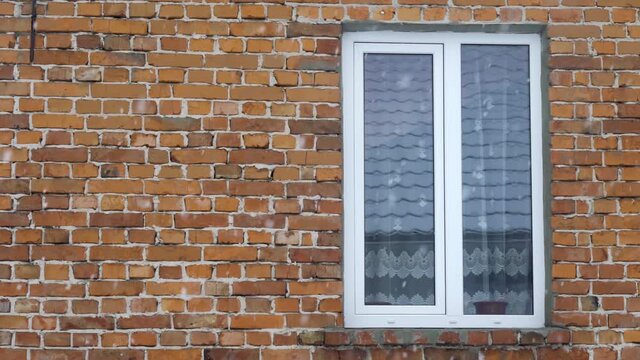 Winter boring dramatic scene, falling snow on the background of a red brick wall. The window in the Side. Slow motion.