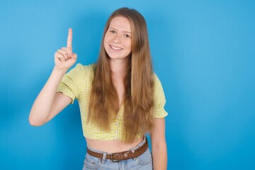 young beautiful blonde woman standing against blue background showing and pointing up with fingers...