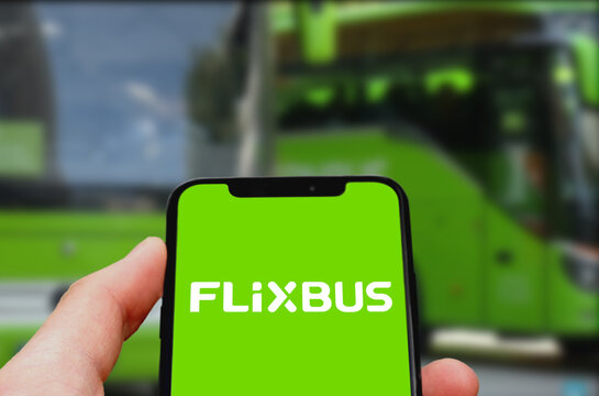 Flixtrain Logo wird auf einem Smartphone angezeigt, dahinter zwei Busse der Flixmobility GmbH an einer Haltestelle, Linienverkehr mit Fernbussen, Reisen, Fernverkehr, Fernbusverkehr