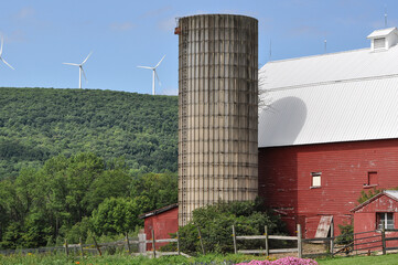 Red barn and silo near the mountains with windmills in the distance.