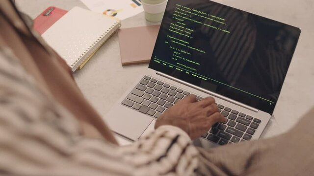 High-angle close-up of unrecognizable male IT student writing programming code on laptop in classroom