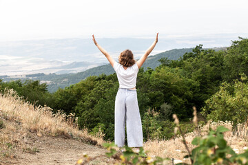 Young woman outdoors in the mountains with open arms, hugs nature, happiness