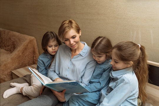 a happy mother with three daughters reads a fairy tale book before going to bed from the bedroom. happy family, reading a book aloud to children, the process of teaching and raising children