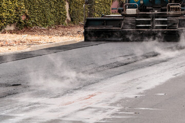 Street paving work with permanent asphalt, with smoke from the heat of the asphalt mass highlighted in the image.
