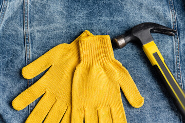 top view of yellow work gloves near hammer on blue denim cloth, labor day concept