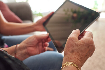 Close-up shot of the hands of an older woman and a young woman holding a digital talbet