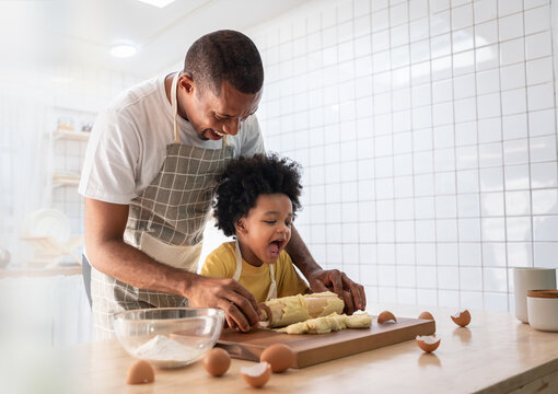 Happy Smiling African American Father and Adorable Son have fun Cooking and kneading dough in white kitchen. Playful Black Family baking cookies together