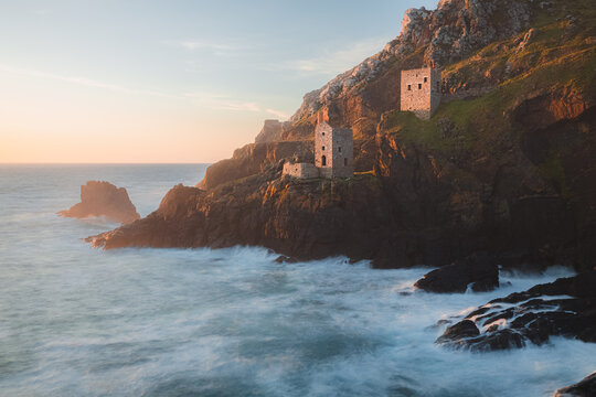 Dramatic seascape landscape of old stone ruins of engine houses at Botallack mines on the Atlantic coast of Cornwall, England, UK during golden hour at sunset or sunrise.